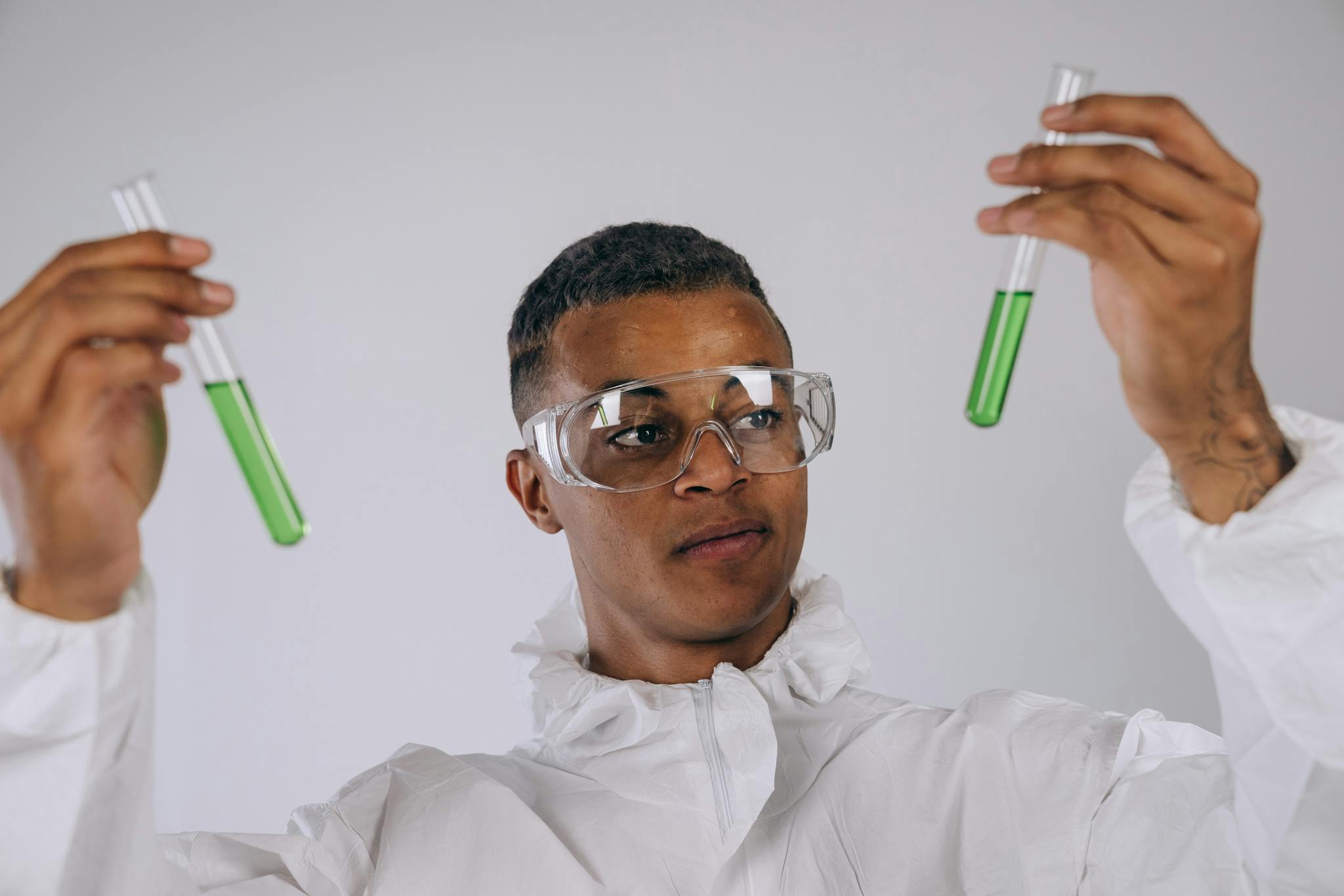 Scientist in protective gear examining green liquid in test tubes.